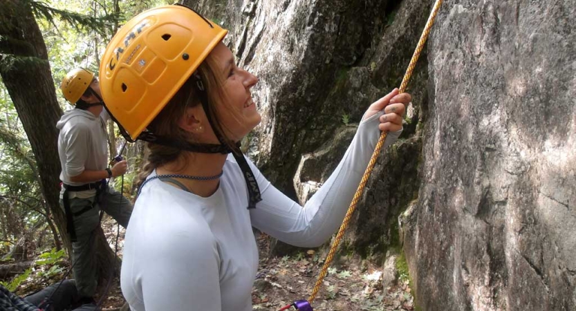 A person wearing a helmet looks up while holding onto a rope, belaying a climber